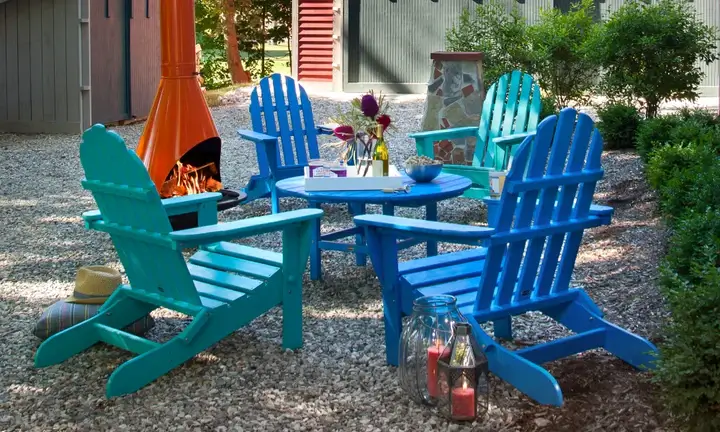 Colorful Adirondack chairs around recycled plastic table by fire pit creating inviting campground seating area that enhances guest comfort and outdoor experience